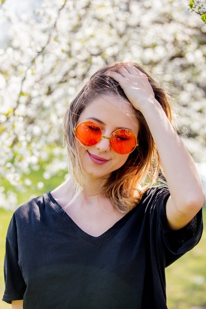 Young girl in a sunglasses stay near a flowering tree in the park. Spring season