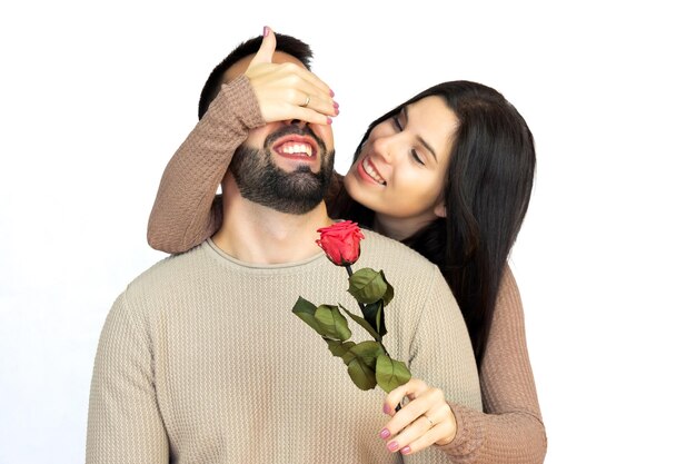 Young girl surprising her partner by covering his eyes with her hand while giving him a rose