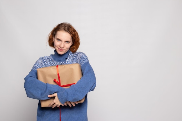 Young girl in a sweater is holding a gift on a white background