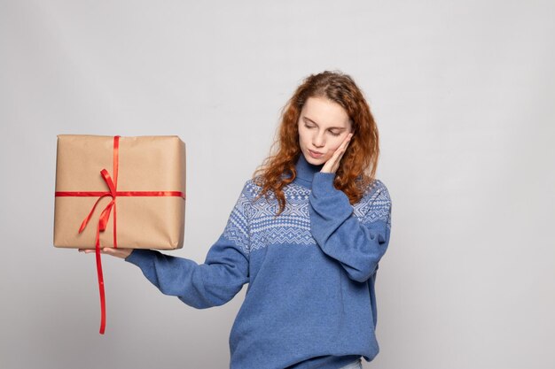 Young girl in a sweater is holding a gift on a white background