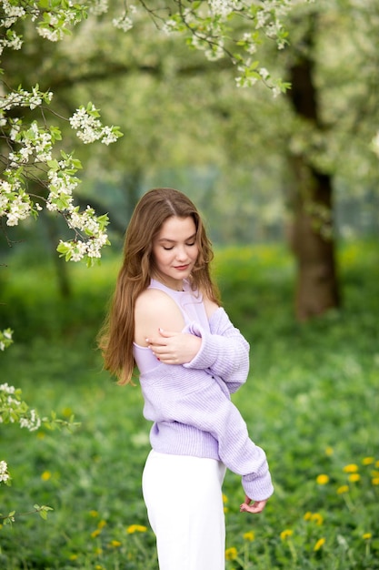 A young girl in a sweater next to white flowers on a tree