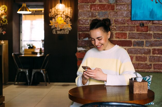 카페 테이블에있는 어린 소녀가 전화 미소와 문자 메시지를 본다