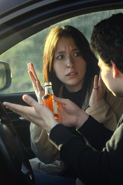 a young girl takes away a bottle of alcohol from her boyfriend while driving a car