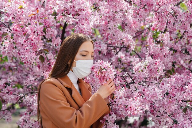 화창한 봄날 전염병이 종식된 후 꽃이 만발한 정원 앞에서 어린 소녀가 마스크를 벗고 심호흡을 하고 있습니다. 보호 및 예방 covid 19.