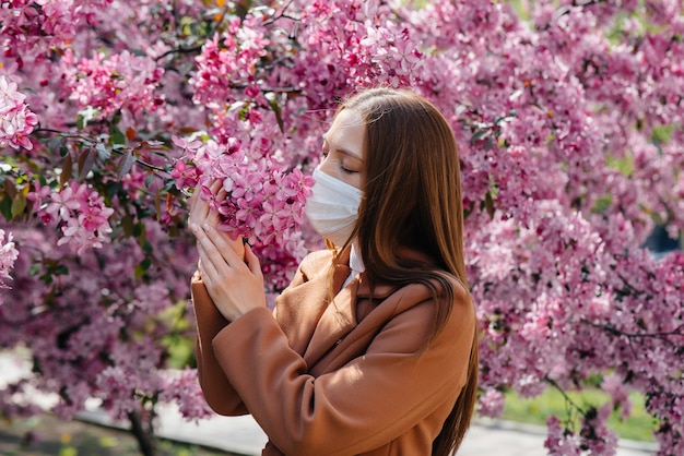 A young girl takes off her mask and breathes deeply after the end of the pandemic on a Sunny spring day, in front of blooming gardens. Protection and prevention covid 19.