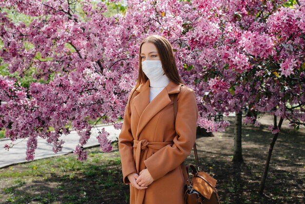 A young girl takes off her mask and breathes deeply after the\
end of the pandemic on a sunny spring day, in front of blooming\
gardens. protection and prevention covid 19.