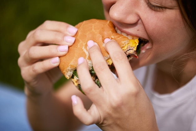 A young girl takes out a burger from a paper bag sitting on the green grass