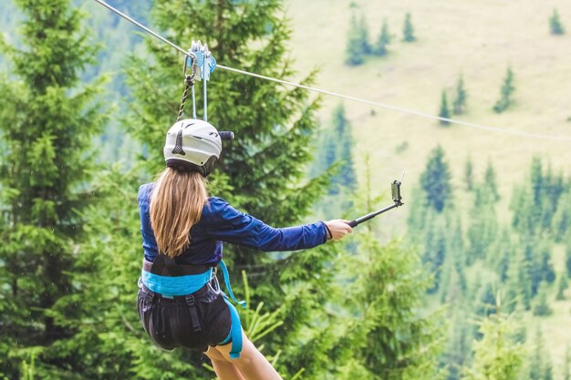 A young girl takes a picture of herself on a cellphone while descending on a zipline