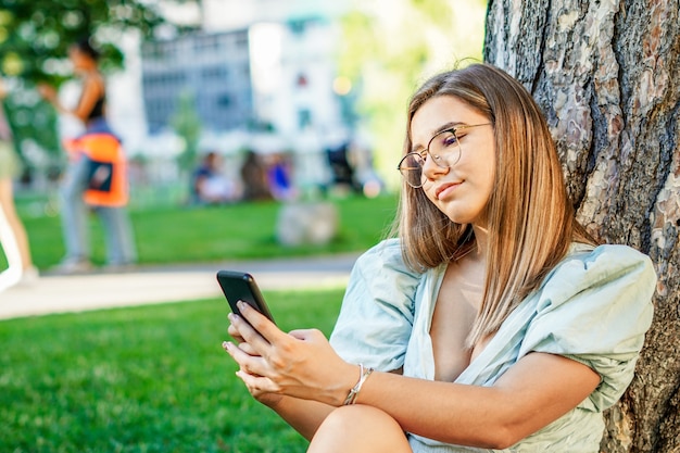 Молодая девушка делает селфи - Подросток держит смартфон в парке - Красивый подросток использует технологии на природе - Летняя атмосфера