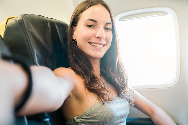 Ragazza che si fa selfie con lo smartphone mentre è seduto sull'aereo