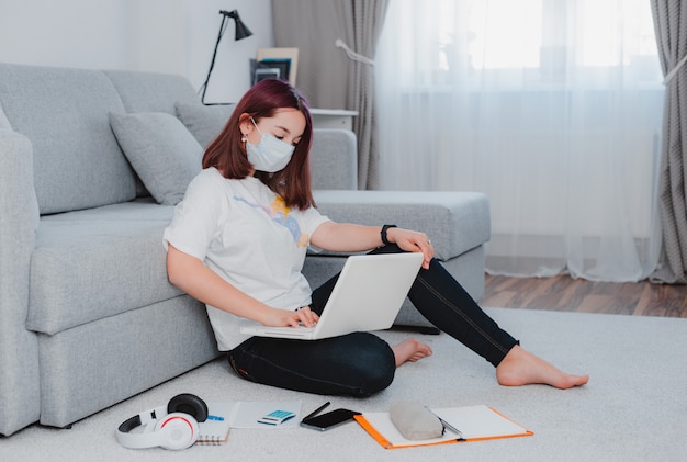 Young girl teenage girl on the floor wearing protective mask using laptop