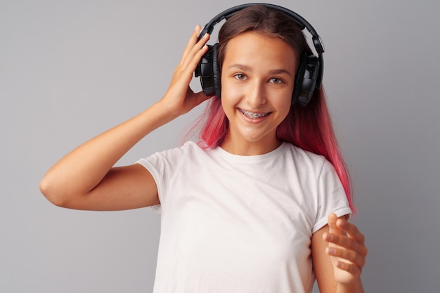 Young girl teenager listening to music with her headphones over a grey background 