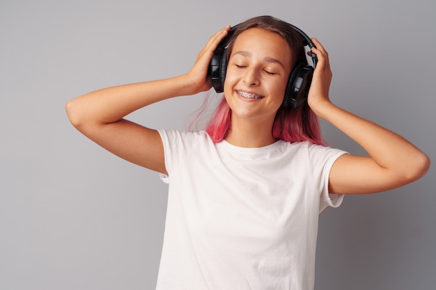 Young girl teenager listening to music with her headphones over a grey  