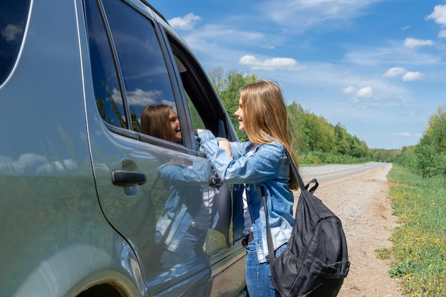 A young girl a teenager with a backpack hitchhiker stopped a car for traveling talking to the