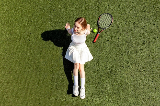 Foto giovane giocatrice di tennis in uniforme sportivo bianco con racchetta da tennis giace e si riposa sul campo verde