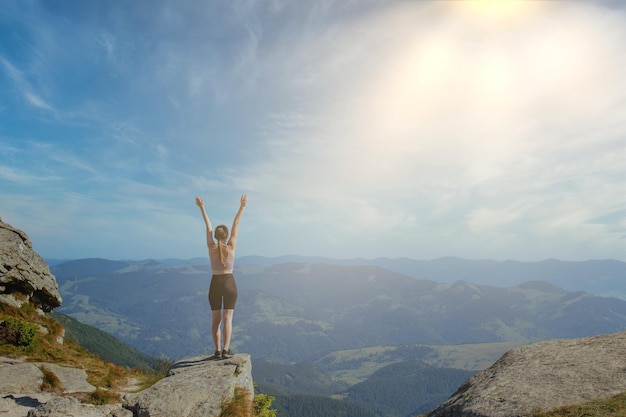 The young girl at the top of the mountain raised her hands up\
on blue sky background the woman climbed to the top and enjoyed her\
success back view