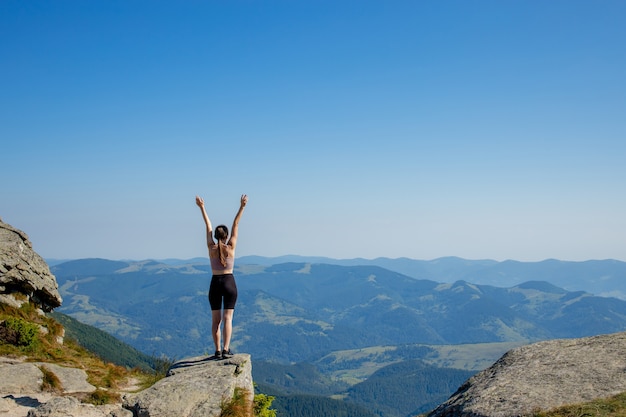 Foto la ragazza in cima alla montagna alzò le mani sul cielo blu. la donna è salita in cima e ha goduto del suo successo. vista posteriore.