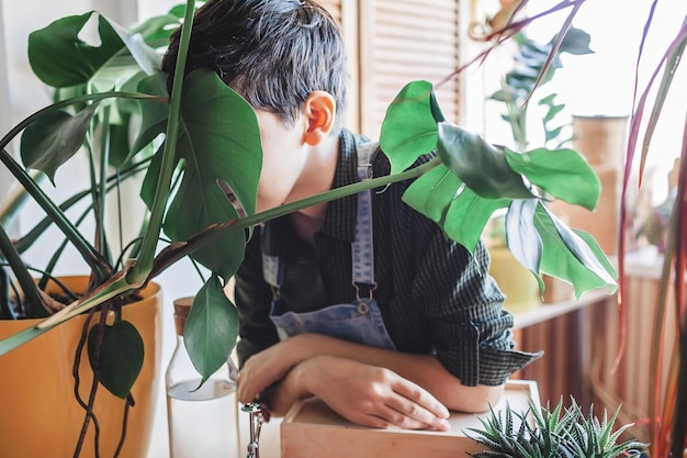 A young girl touches her face with green leaf to relax and detox home plants on the balcony