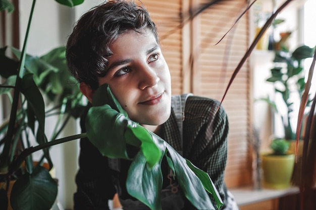 A young girl touches her face with green leaf to relax and detox home plants on the balcony