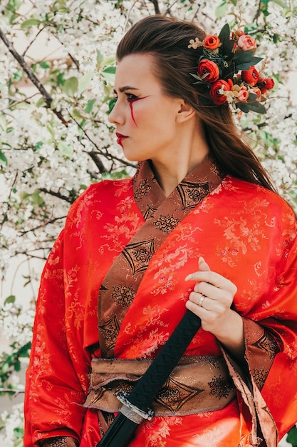 Young girl in traditional kimano in a blooming garden with samurai japanese sword katana in image of warrior woman