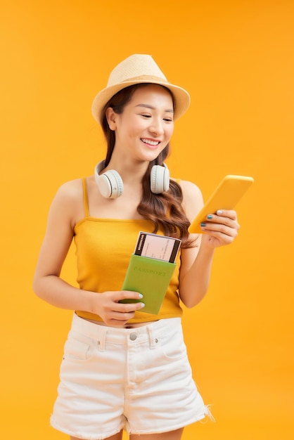 Young girl traveller holding passport and using smartphone over orange background