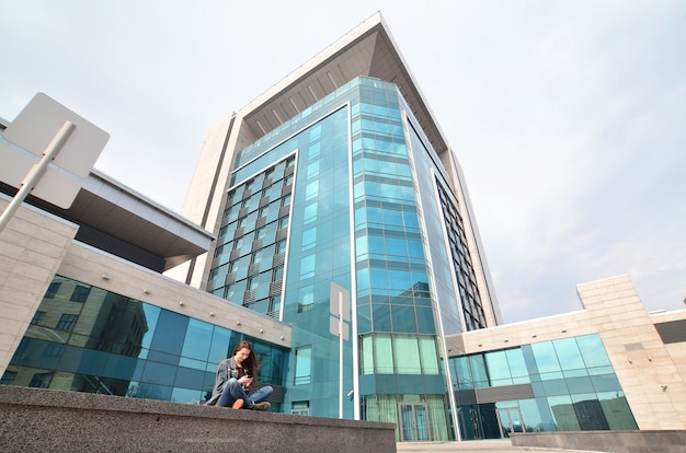 Young girl uses a smartphone on the office building background