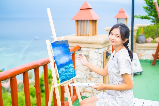 Молодая девушка рисует кистью на холсте с красивым пейзажным видом на ко тао, Таиланд