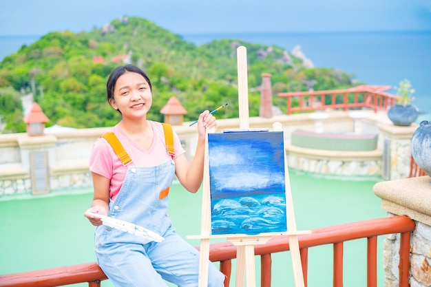 Молодая девушка рисует кистью на холсте с красивым пейзажным видом на ко тао, Таиланд