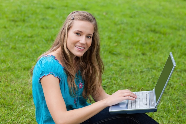 Молодая девушка, используя свой ноутбук в парке, глядя на камеру