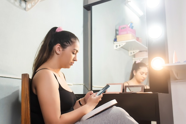 Young girl using her smartphone in front of her makeup vanity.