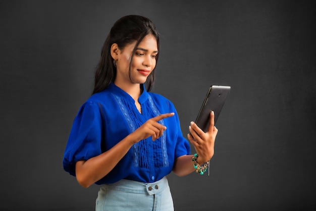 Ragazza che utilizza il telefono cellulare o lo smartphone su sfondo grigio