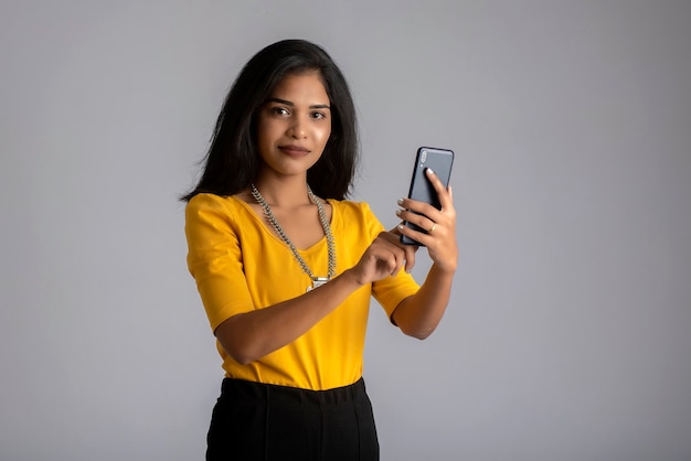 Young girl using mobile phone or smartphone on gray wall