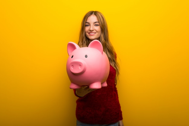 Young girl on vibrant yellow background holding a piggybank
