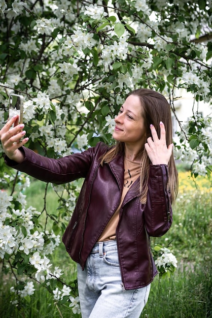 A young girl walking in the park makes a video call on a smartphone and laughs the spring season apple tree blossoms people use technology