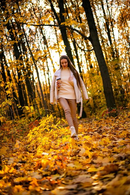 Young girl walks in the autumn park and holds cup of coffee in her hands young girl walks in the autumn park and holds cup of coffee in her hands