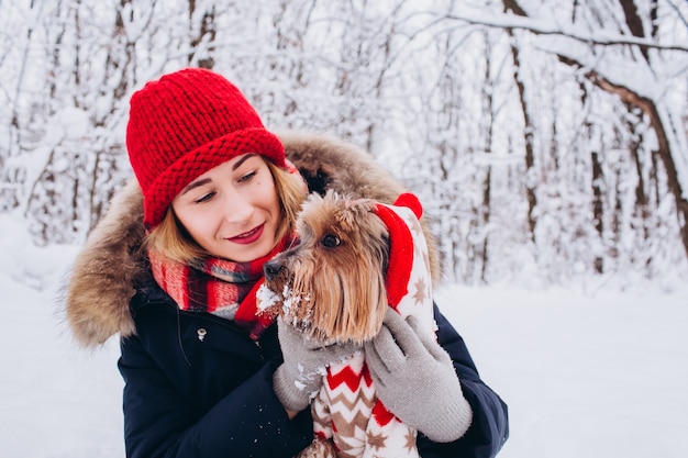 若い女の子は、クリスマスセーターを着て犬と一緒に冬に低い森の中を歩きます