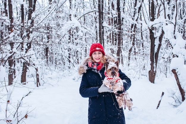 Young girl walks in the lower woods in winter with dog wearing a christmas sweater