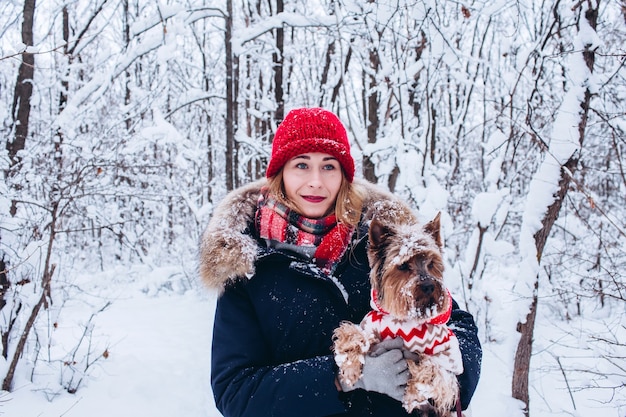 Young girl walks in the lower woods in winter with dog wearing a christmas sweater