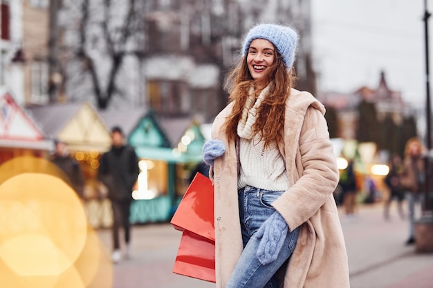 Young girl in warm clothes with shopping bags in hands have a walk outdoors in the city.