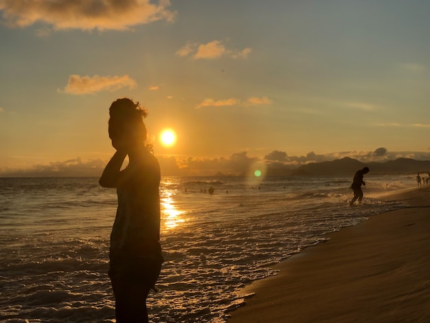 ブラジル、リオデジャネイロのバラダチジュカビーチで夕日を見ている少女。穏やかな波の海。