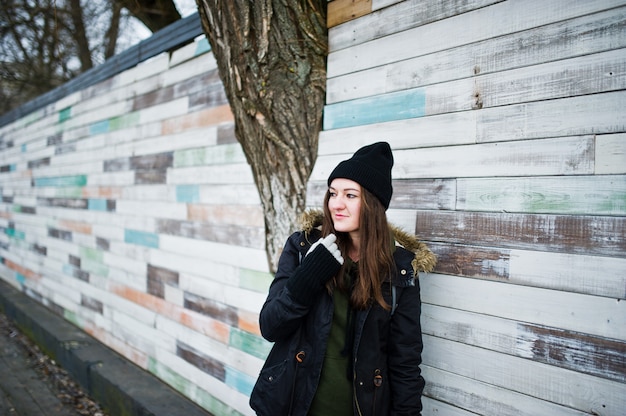 Young girl wear black headwear against wooden wall.