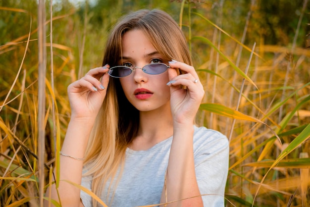 Photo young girl wearing blank gray tshirt and black jeans in blue glasses posing against high grass