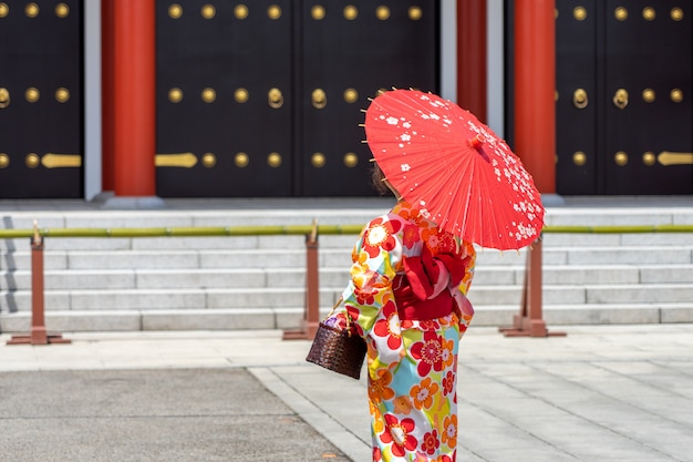 Молодая девушка в японском кимоно стоит перед храмом Сэнсодзи в Токио,