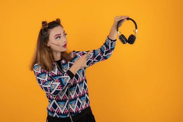 Young girl wearing makeup and holding headphones on yellow background. High quality photo