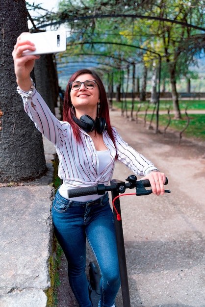 Young girl wearing a shirt and headphones taking a selfie riding a scooter