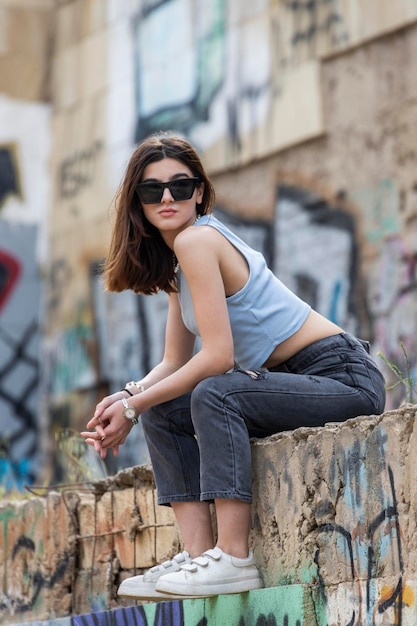 Молодая девушка в солнечных очках сидит на городской улице