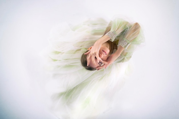 Young girl in a wedding dress is kneeling with her arms thrown up and looking through her fingers