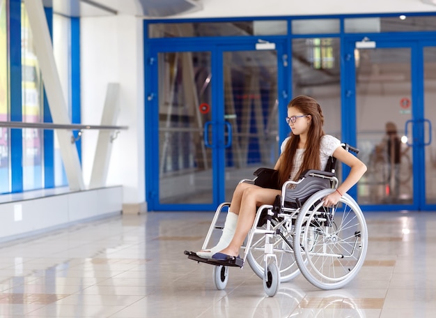 A young girl in a wheelchair is standing in the corridor of the hospital.