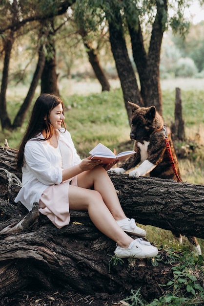 Young girl in white clothes sits on a tree in the forest and reads a book