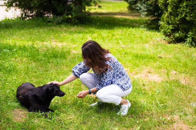 A young girl in white jeans plays with a black dog in the street. Outdoor recreation, walk in the park with the dog. Close-up.